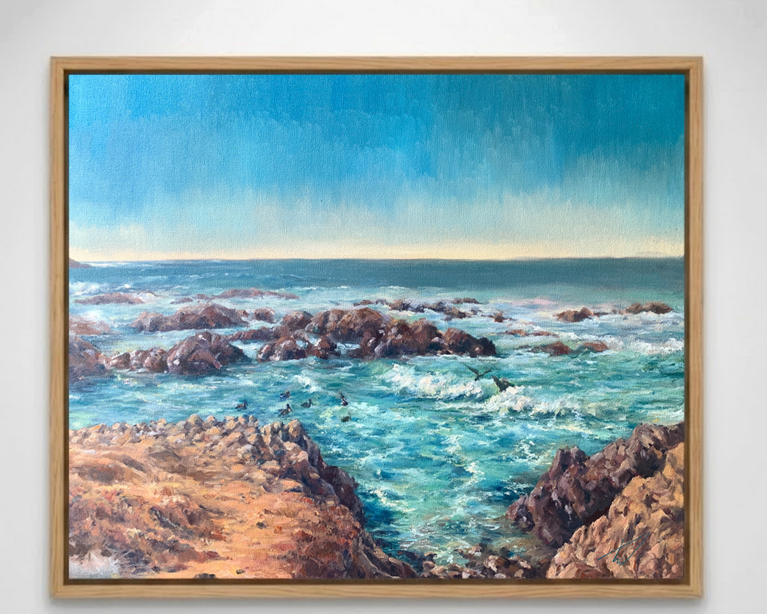Framed painting of a coastal scene with rocky shoreline and blue sky.